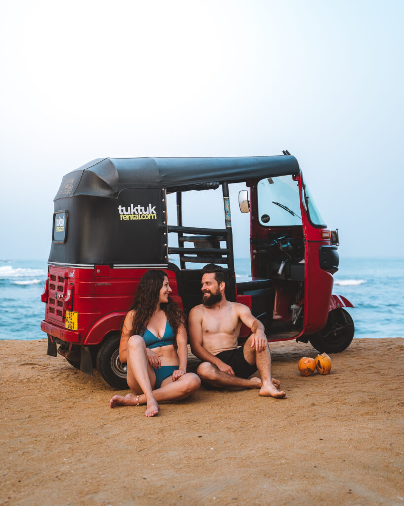 A couple who has parched their tuktuk close to beach and drinking king coconut