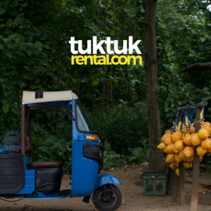 A woman drinks a king coconut next to a blue tuk-tuk.
