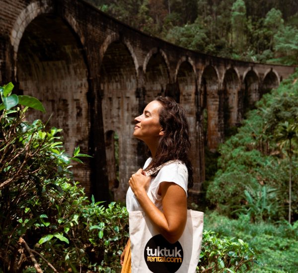 Lady with a Tuk Tuk Rental bag in front of an arch bridge.